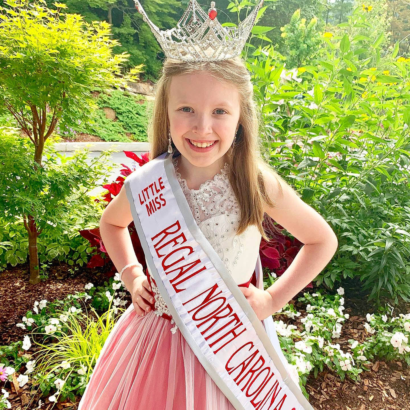 Caylee is registered to the contest to win money with this photo: blond, clothing, costume, costume_accessory, crown, dress, fashion_accessory, hair_accessory, happy, headgear, headpiece, joy, person, plant, sash, smile