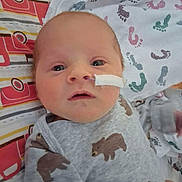 John is registered to the contest to win money with this photo: baby, newborn, infant, onesie, bear_print, medical_tape, nasal_tube, bed, blanket, footprint_pattern, face, head, person, clothing, cute, lying_down, indoor, closeup, soft_lighting, expression