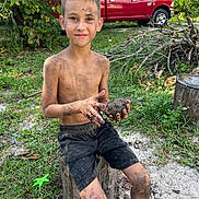 Daniel is registered to the contest to win money with this photo: boy, child, mud, dirt, outdoor, nature, tree_stump, grass, shorts, barefoot, greenery, truck, branches, summer, play, happy, messy, portrait, smiling, sunlight