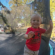 Mark joined the competition — help win amazing prizes! backyard, beige_shorts, casual_clothing, child, daylight, grass, happy, mesh, outdoor, person, playing, reaching, red_shirt, safety_net, smiling, summer, sunny, toddler, trampoline, trees