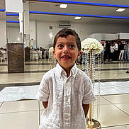 Imran participe au concours pour gagner de l'argent avec cette photo : child, boy, white_shirt, smile, indoor, event, flower_arrangement, people, formal, floor_tiles, group, celebration, decor, happy, portrait, standing, hands_behind_back, short_hair, casual, lighting