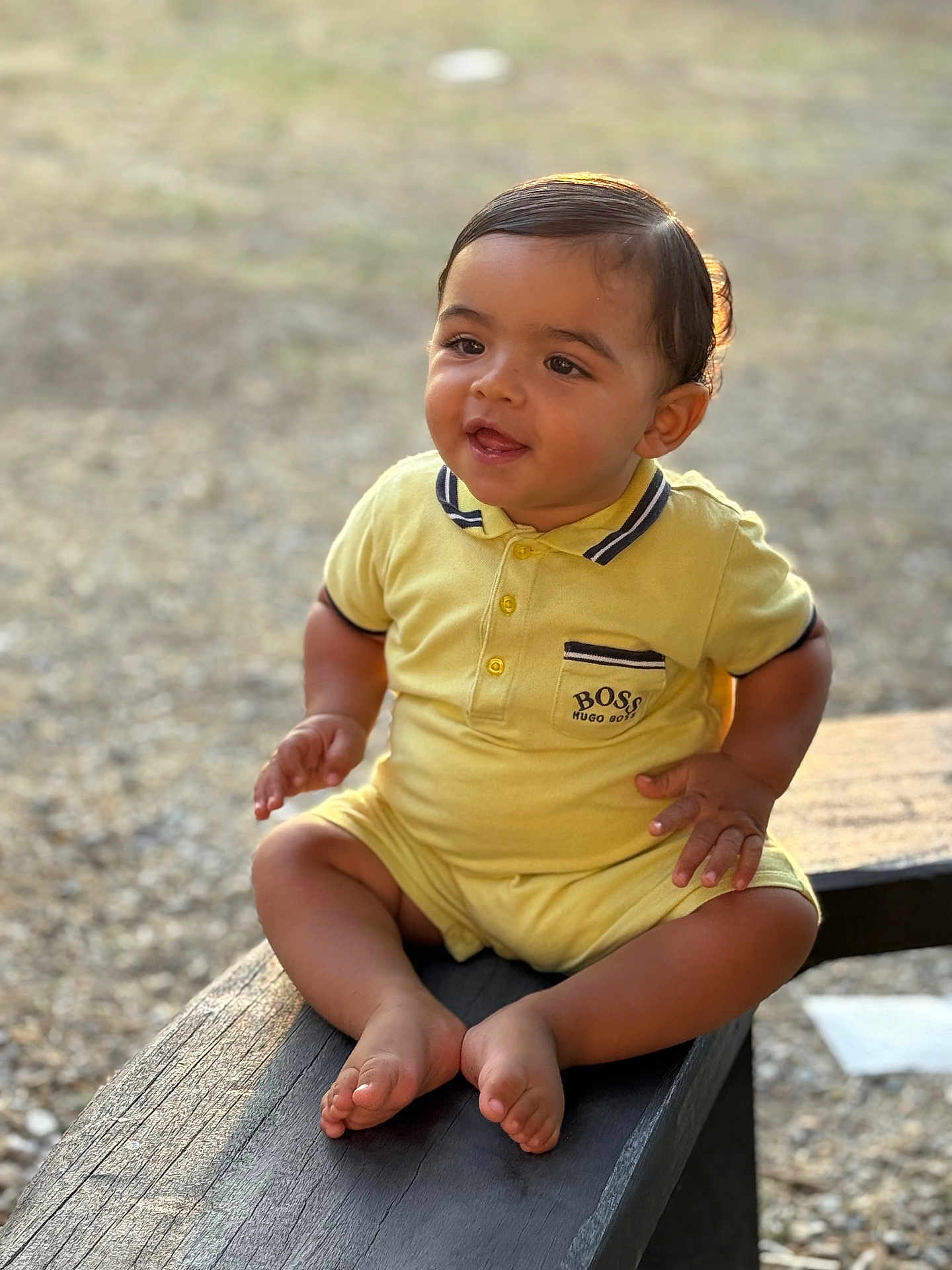 Zayd participe au concours pour gagner de l'argent avec cette photo : baby, child, yellow_outfit, sitting, bench, outdoor, natural_light, happy, curious, portrait, head, face, feet, wood, sunlight, smile, infant, young_child, casual_clothing, nature