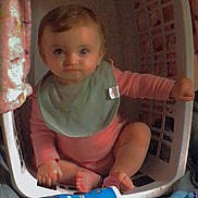 Addison is registered to the contest to win money with this photo: baby, laundry_basket, infant, child, toy, plush_toy, floor, bib, clothing, sitting, indoor, curious, bottle, container, pink, blue, carpet, hand, feet, face
