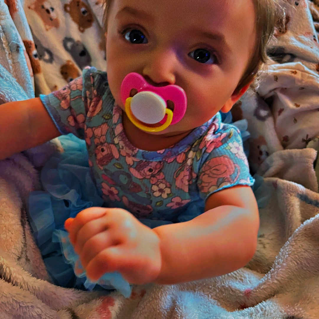 Addison joined the competition — help win amazing prizes! animal_print, baby, blanket, blue_tutu, child, closeup, comfort, cozy, cute, expression, face, floral_dress, hand, indoors, infant, pacifier, person, portrait, soft_texture, young_child