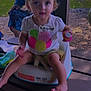 toddler, child, booster_seat, pacifier, outdoor, picnic_table, person, grass, tree, shirt, name_tag, birthday, summer, daylight, cute, sitting, baby, parent, play, nature