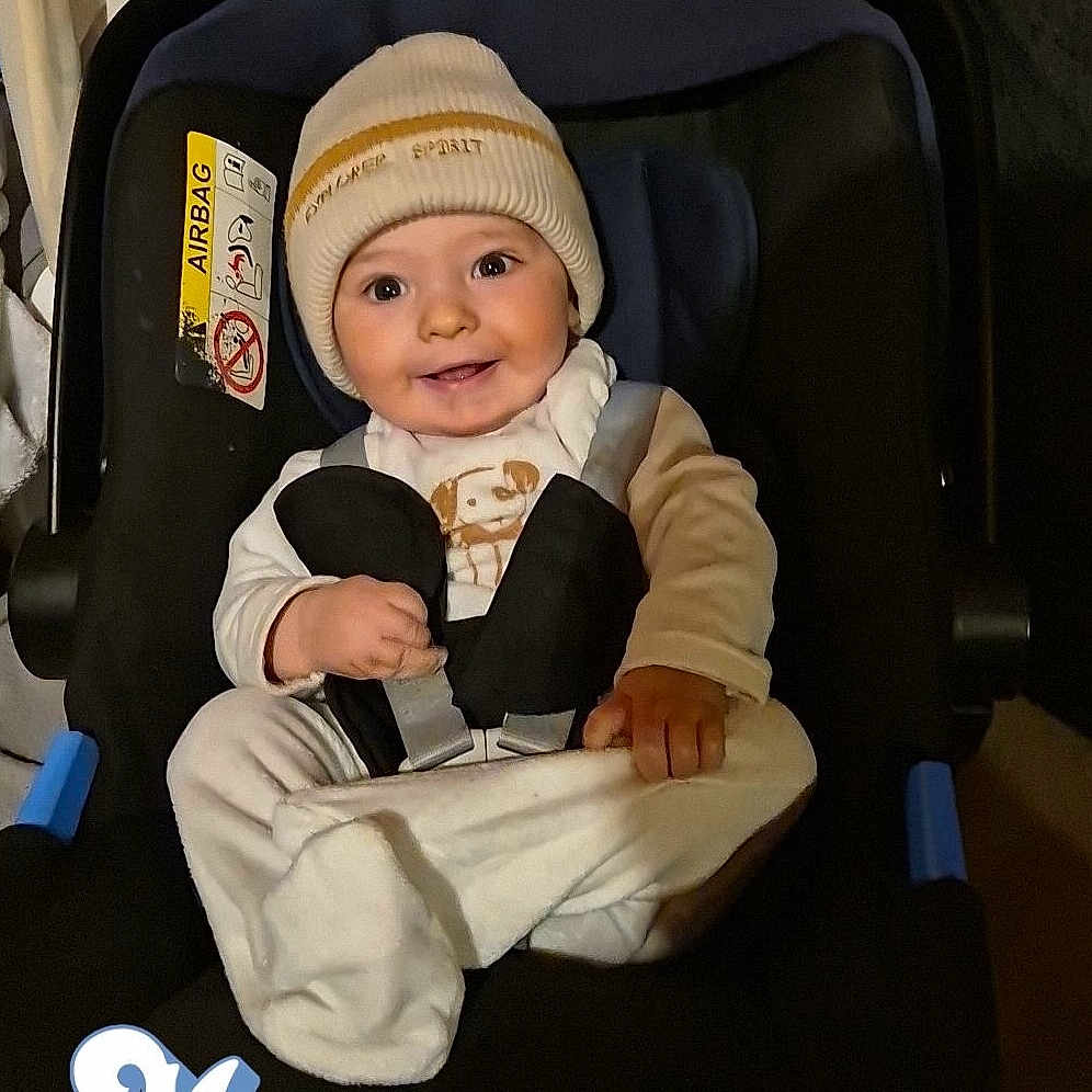 Nino participe au concours pour gagner de l'argent avec cette photo : baby, beanie, car_seat, child, clothing, cozy, cute, face, happy, headwear, indoors, infant, person, portrait, seatbelt, sitting, small_hands, smile, toddler, warm