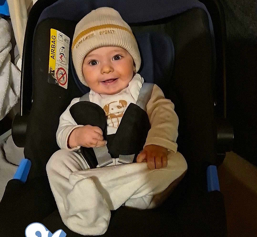 Nino participe au concours pour gagner de l'argent avec cette photo : baby, car_seat, beanie, smile, clothing, child, infant, seatbelt, cute, portrait, indoors, person, happy, warm, sitting, face, headwear, toddler, small_hands, cozy