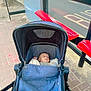 baby, stroller, infant, blue, blanket, bus_stop, bench, red, sidewalk, street, urban, outdoor, child, peaceful, waiting, transportation, pavement, canopy, daytime, casual