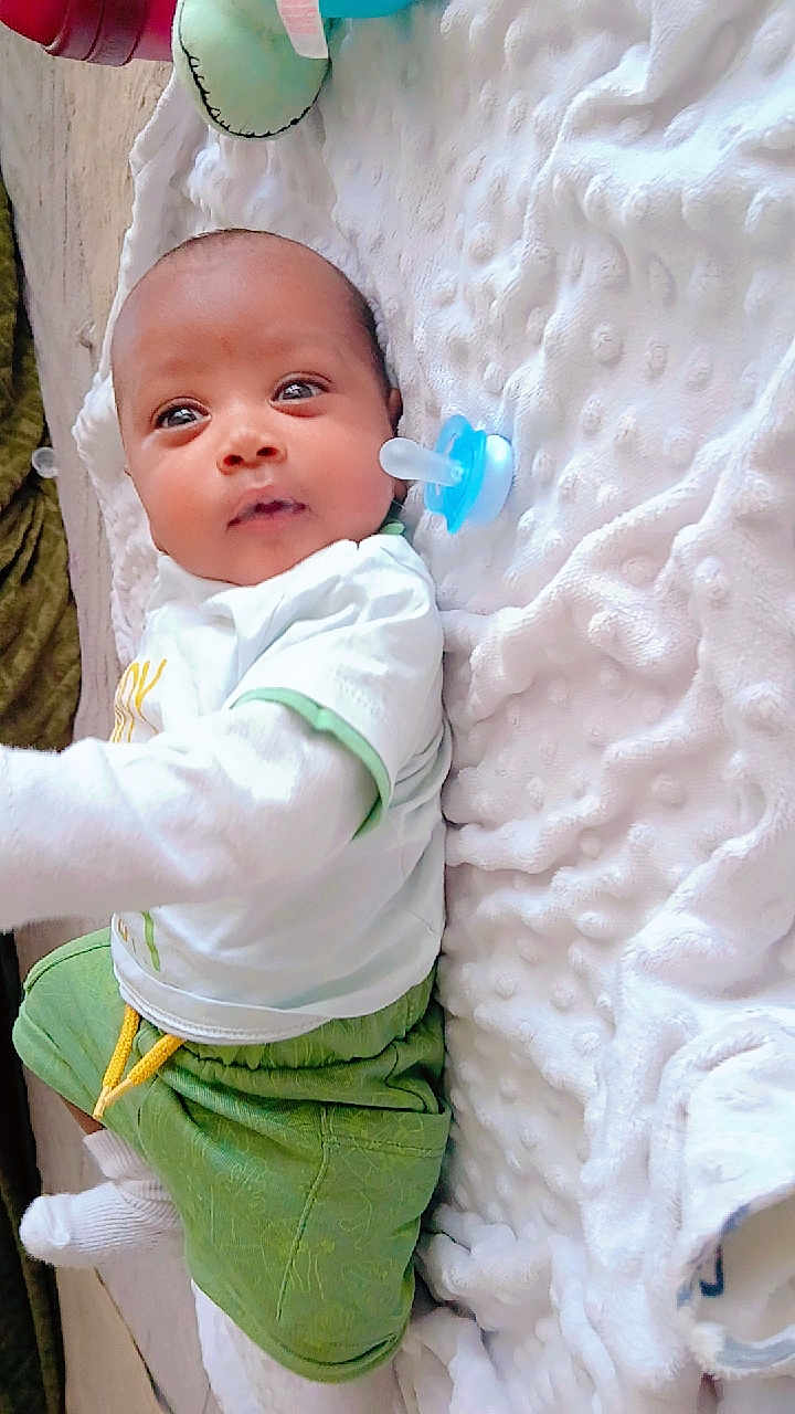 Ibrahim participe au concours pour gagner de l'argent avec cette photo : baby, infant, child, pacifier, blanket, white_blanket, green_shorts, white_shirt, lying_down, indoors, soft_texture, cute, small_person, sleepwear, socks, infant_clothing, portrait, baby_boy, young_child, resting