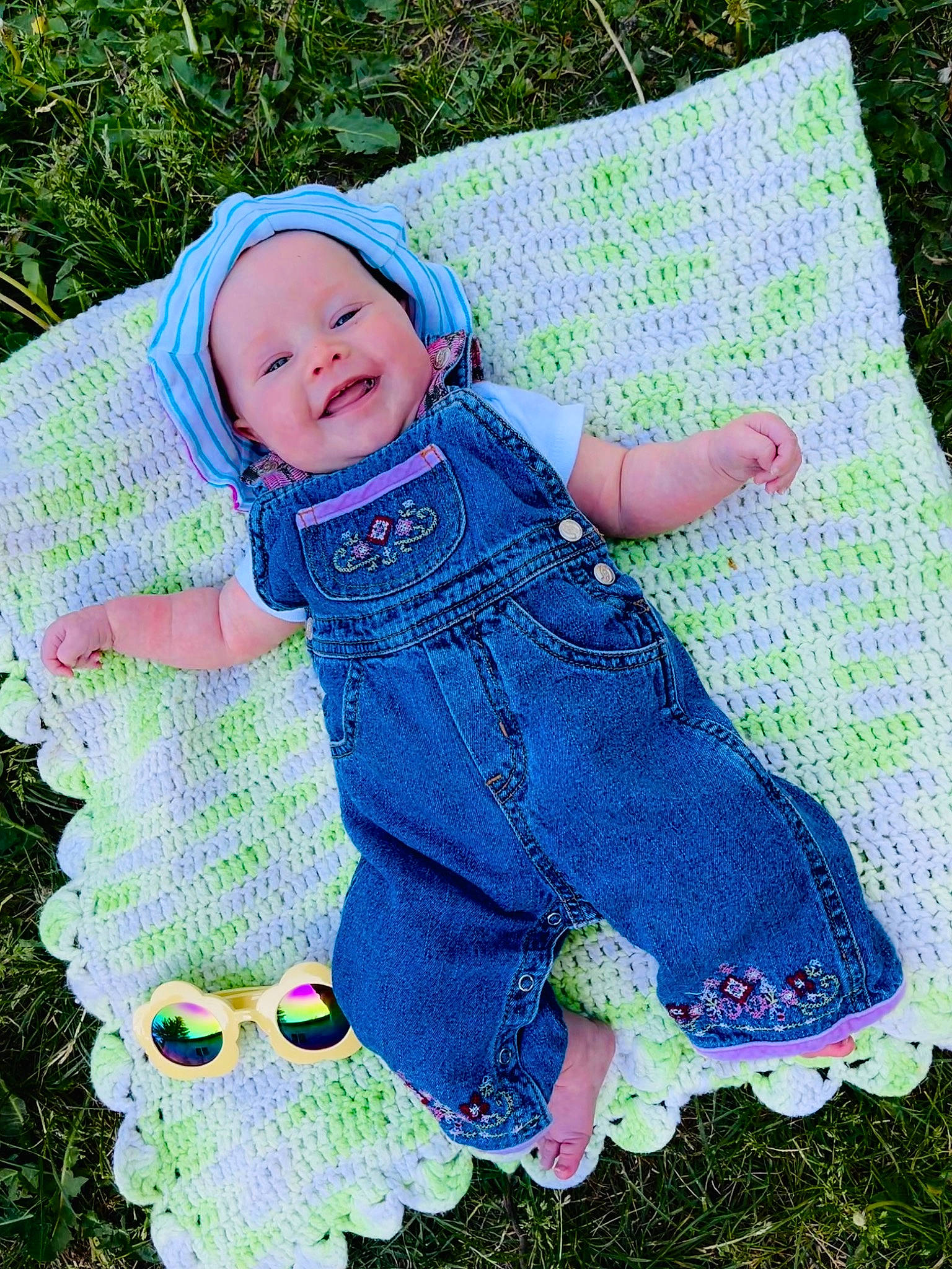 Kairi is registered to the contest to win money with this photo: baby, baby_products, baby_toddler_clothing, child, denim, electric_blue, fashion_accessory, grass, green, happy, headwear, magenta, pattern, people_in_nature, person, purple, sitting, sleeve, smile, textile