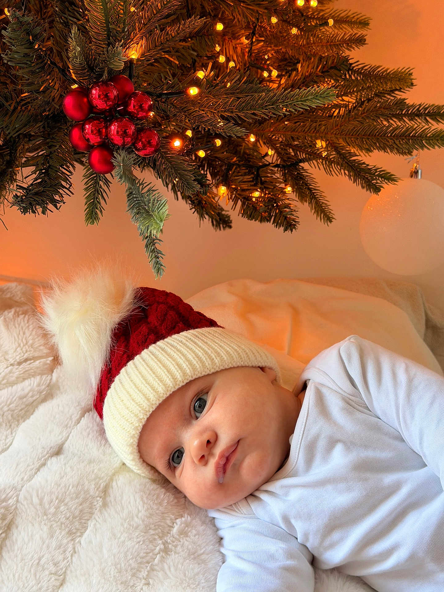 Marcus is registered to the contest to win money with this photo: baby, infant, christmas_hat, red_hat, white_hat, blanket, christmas_tree, pine_branches, christmas_lights, red_ornaments, holiday, festive, cozy, indoors, cute, child, portrait, sleepwear, soft_texture, holiday_decor