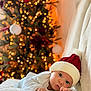 Marcus is registered to the contest to win money with this photo: baby, infant, hat, red_hat, white_clothing, blanket, christmas_tree, lights, bokeh, holiday, festive, cozy, cute, portrait, indoor, child, face, blue_eyes, soft_texture, seasonal