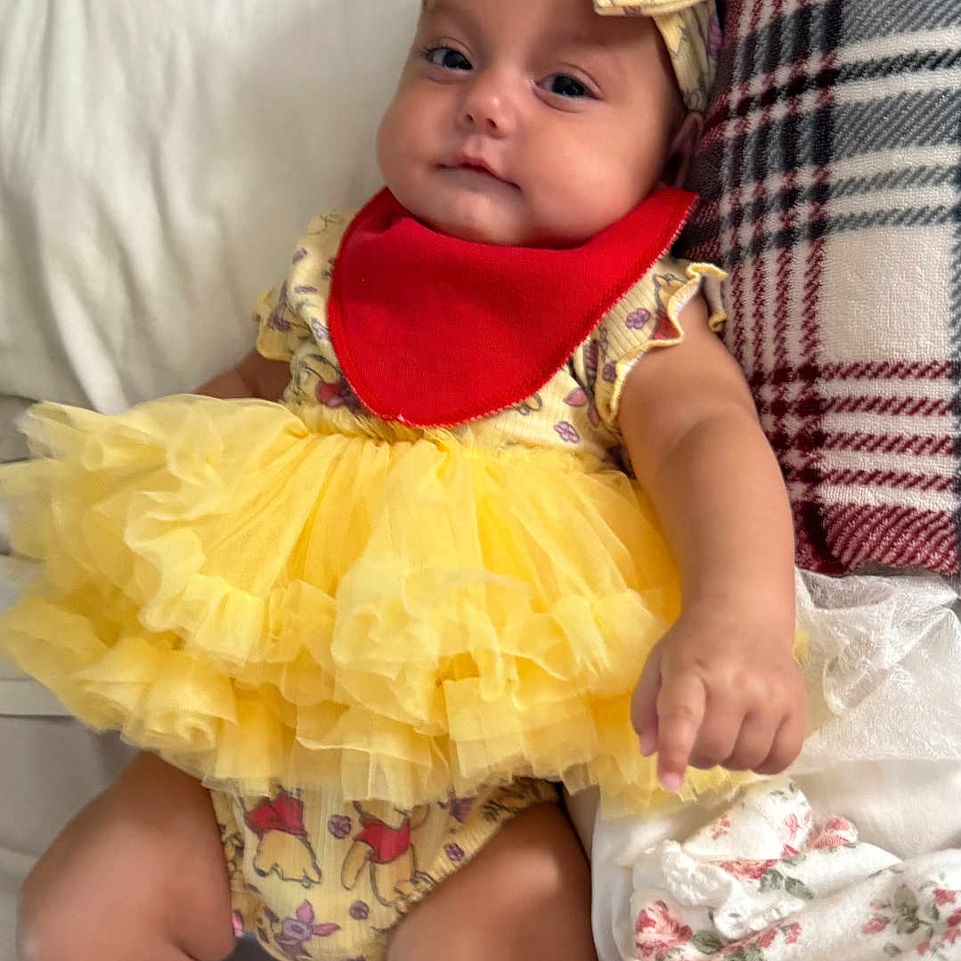 Bellatrix joined the competition — help win amazing prizes! arm, baby, blanket, child, clothing, couch, cozy, cute, face, headband, indoors, infant, legs, plaid, portrait, red_bib, sitting, smiling, soft_toys, yellow_dress