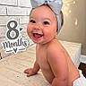 baby, infant, child, smiling, happy, portrait, sitting, bow, headband, diaper, milestone, eight_months, indoor, mattress, bedroom, brick_wall, warm_lighting, photography, text_overlay, closeup