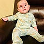 baby, child, pajamas, cartoon_pattern, sitting, chair, leather, indoor, cute, infant, young_child, clothing, face, portrait, relaxing, home, furniture, cozy, curious, smiling