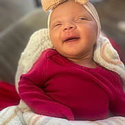 Kallie is registered to the contest to win money with this photo: baby, infant, smile, headband, bow, blanket, red_clothing, cozy, cute, portrait, child, happy, indoors, soft_texture, closeup, newborn, sleepy, wrapped, person, warm