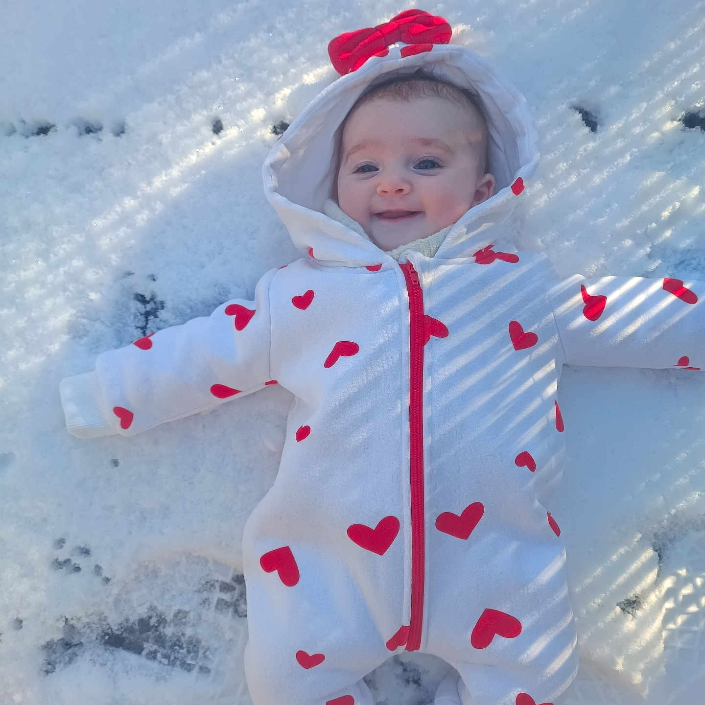 Amélia a rejoint le concours — aidez-le/la à gagner de superbes lots ! baby, child, clothing, cold_weather, cute, face, footwear, happy, heart_pattern, hood, infant, onesie, outdoor, person, red_bow, smile, snow, snowy_ground, warm_clothes, winter