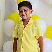 Eymen Asaf participe au concours pour gagner de l'argent avec cette photo : child, boy, yellow_clothing, smile, balloons, party, celebration, yellow_balloon, white_balloon, flower_balloon, shorts, buttoned_shirt, standing, happy, indoor, portrait, festive, decorations, cute, casual