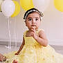 Elif a rejoint le concours — aidez-le/la à gagner de superbes lots ! baby, child, yellow_dress, daisy_pattern, headband, balloons, yellow_balloons, white_balloons, sitting, indoor, floor, cute, portrait, celebration, festive, toddler, flower_accessory, happy, person, smile