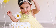 Elif a rejoint le concours — aidez-le/la à gagner de superbes lots ! baby, child, birthday, cake, balloons, yellow_dress, flower_headband, celebration, daisy_pattern, smiling, sitting, indoor, first_birthday, happy, decorations, party, cute, infant, food, photography