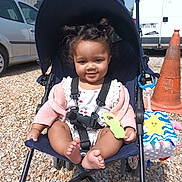 Manon a rejoint le concours — aidez-le/la à gagner de superbes lots ! child, toddler, stroller, outdoor, toy, smile, cute, hair, gravel, car, traffic_cone, sunlight, clothing, seatbelt, playful, baby, happy, person, daylight, accessory