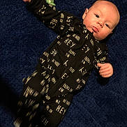 Preston Kjeldgard is registered to the contest to win money with this photo: baby, infant, child, portrait, lying_down, blue_rug, black_outfit, printed_clothing, hey_text, waving, fist, bald, eyes_open, curious, indoors, soft_surface, full_body, casual, photograph, cute