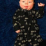 baby, child, infant, portrait, lying_down, smiling, tongue_out, raised_hand, black_outfit, jumpsuit, patterned_clothing, letters, blue_blanket, indoor, close_up, face, eyes, hands, cozy, photograph
