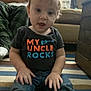 toddler, child, sitting, indoor, carpet, striped_carpet, shirt, text_on_shirt, person, baby, adult, couch, living_room, hand, hair, denim_jeans, expression, curly_hair, home, casual_clothing