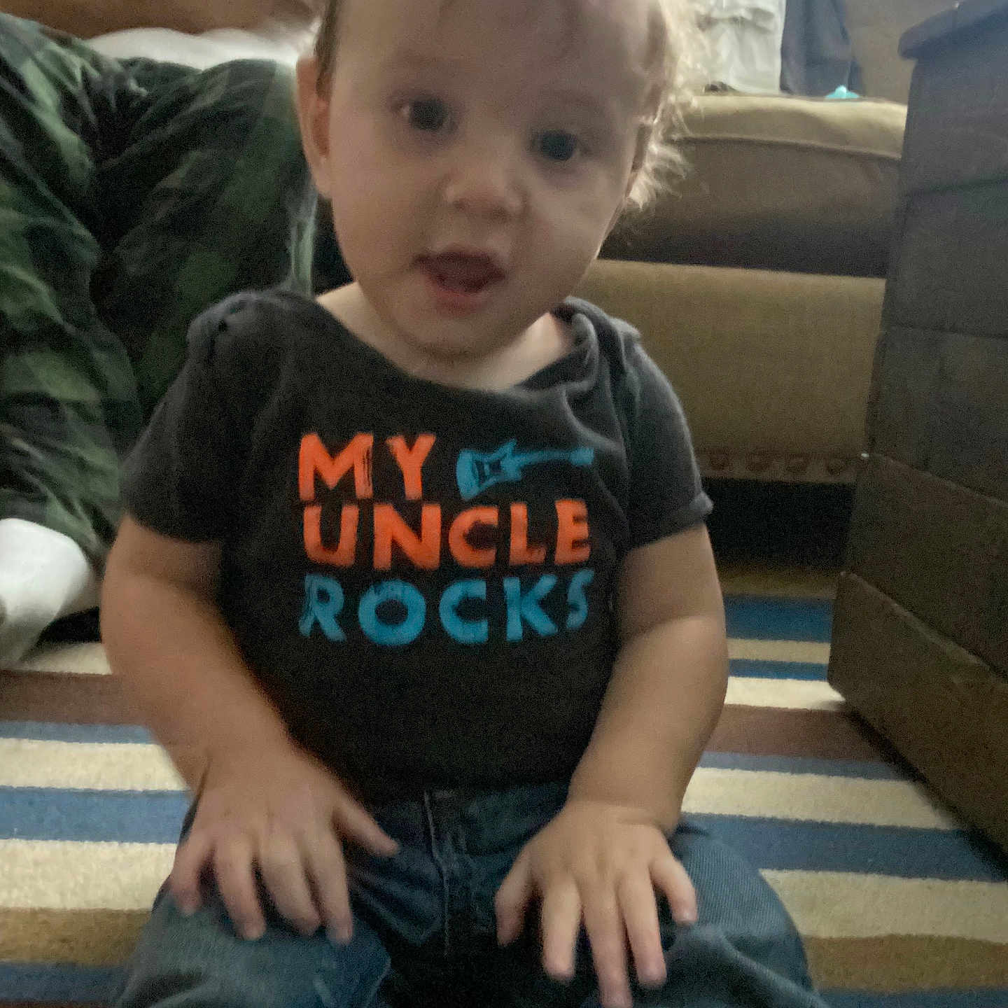 Zeke joined the competition — help win amazing prizes! adult, baby, carpet, casual_clothing, child, couch, curly_hair, denim_jeans, expression, hair, hand, home, indoor, living_room, person, shirt, sitting, striped_carpet, text_on_shirt, toddler
