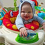 baby, child, smiling, hooded_clothing, activity_center, toy, outdoor, grass, playtime, colorful, happy, infant, cute, person, sitting, sunny, daytime, hand, footwear, play