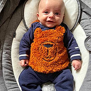 Aaron participe au concours pour gagner de l'argent avec cette photo : apparel, baby, bear_design, blue, child, clothing, comfort, cushion, cute, face, fuzzy, happy, indoors, infant, onesie, orange, person, portrait, seat, smiling