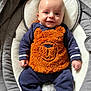 baby, infant, smiling, face, clothing, orange, blue, onesie, fuzzy, bear_design, cushion, seat, comfort, happy, cute, child, portrait, indoors, person, apparel