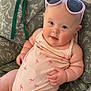 baby, infant, sunglasses, pink_clothing, flamingo_pattern, cushion, chair, indoor, cute, chubby, smiling, face, headwear, person, skin, arm, hand, leg, comfort, relaxing