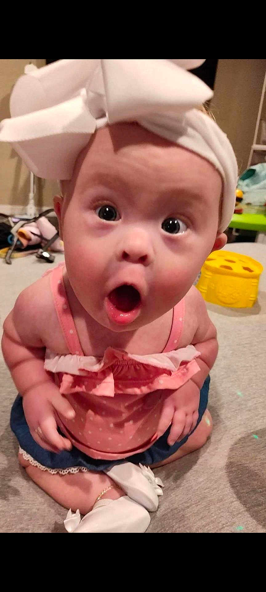 Brooklynne is registered to the contest to win money with this photo: baby, child, surprised, headband, bow, pink_clothing, denim_shorts, white_shoes, sitting, carpet, indoor, wide_eyes, open_mouth, cute, infant, expression, person, floor, toy, background