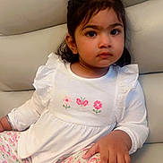 Jasreet is registered to the contest to win money with this photo: toddler, child, girl, sitting, couch, white_top, floral_pants, indoors, casual_clothing, curly_hair, brown_eyes, portrait, cute, young_child, comfortable, relaxed, home, expression, fashion, furniture
