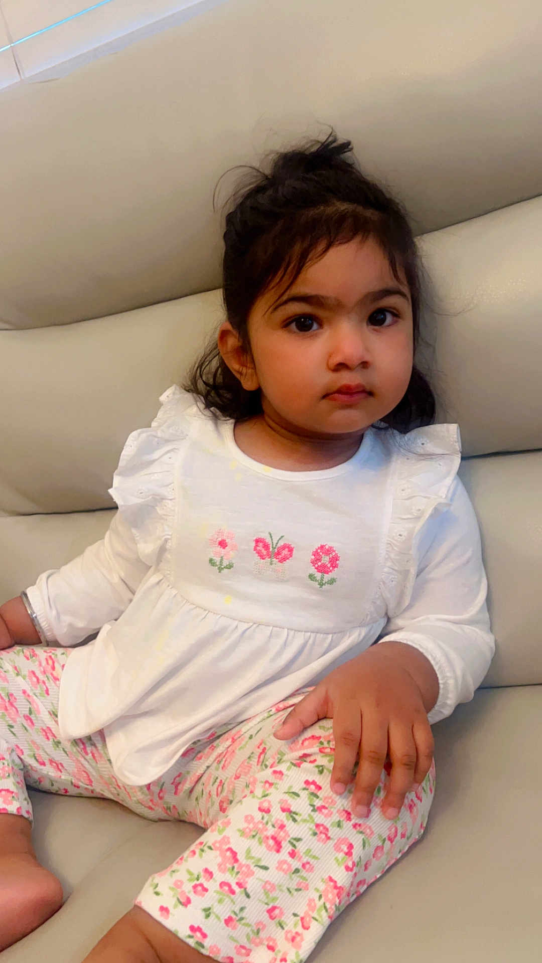 Jasreet is registered to the contest to win money with this photo: toddler, child, girl, sitting, couch, white_top, floral_pants, indoors, casual_clothing, curly_hair, brown_eyes, portrait, cute, young_child, comfortable, relaxed, home, expression, fashion, furniture