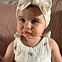 baby, child, headband, bow, dress, white, floral, embroidery, portrait, cute, indoors, soft_light, pink_background, closeup, infant, person, fashion, texture, sitting, curious