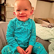 Hunter is registered to the contest to win money with this photo: toddler, child, pajamas, smile, bed, indoor, animal_print, happy, face, hands, clothing, furniture, blanket, room, cute, sitting, person, cozy, portrait, young_child