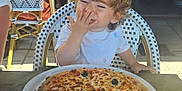 Layana a rejoint le concours — aidez-le/la à gagner de superbes lots ! casual, chair, cheese, child, curly_hair, daylight, food, glass, happy, indoor, olive, person, pizza, plate, restaurant, seat, smiling, table, toddler, white_shirt