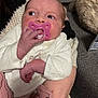 newborn, baby, pacifier, infant, hand, clothing, white_clothing, pink_pacifier, person, couch, cat_tail, adult_hand, indoor, soft_texture, knitwear, closeup, portrait, baby_clothes, resting, cute