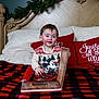 Ariana joined the competition — help win amazing prizes! toddler, child, bed, book, red_pillow, christmas_decor, mickey_mouse, sweater, blanket, plaid, wooden_headboard, smiling, indoors, holiday, face, person, red_clothing, white_pillow, reading, festive
