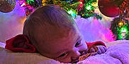 Atticus joined the competition — help win amazing prizes! baby, blanket, christmas_tree, christmas_lights, ornament, decorations, festive, holiday, toddler, face, indoor, cozy, colorful, soft_texture, child, person, warm_lighting, greenery, red_clothing, reflection