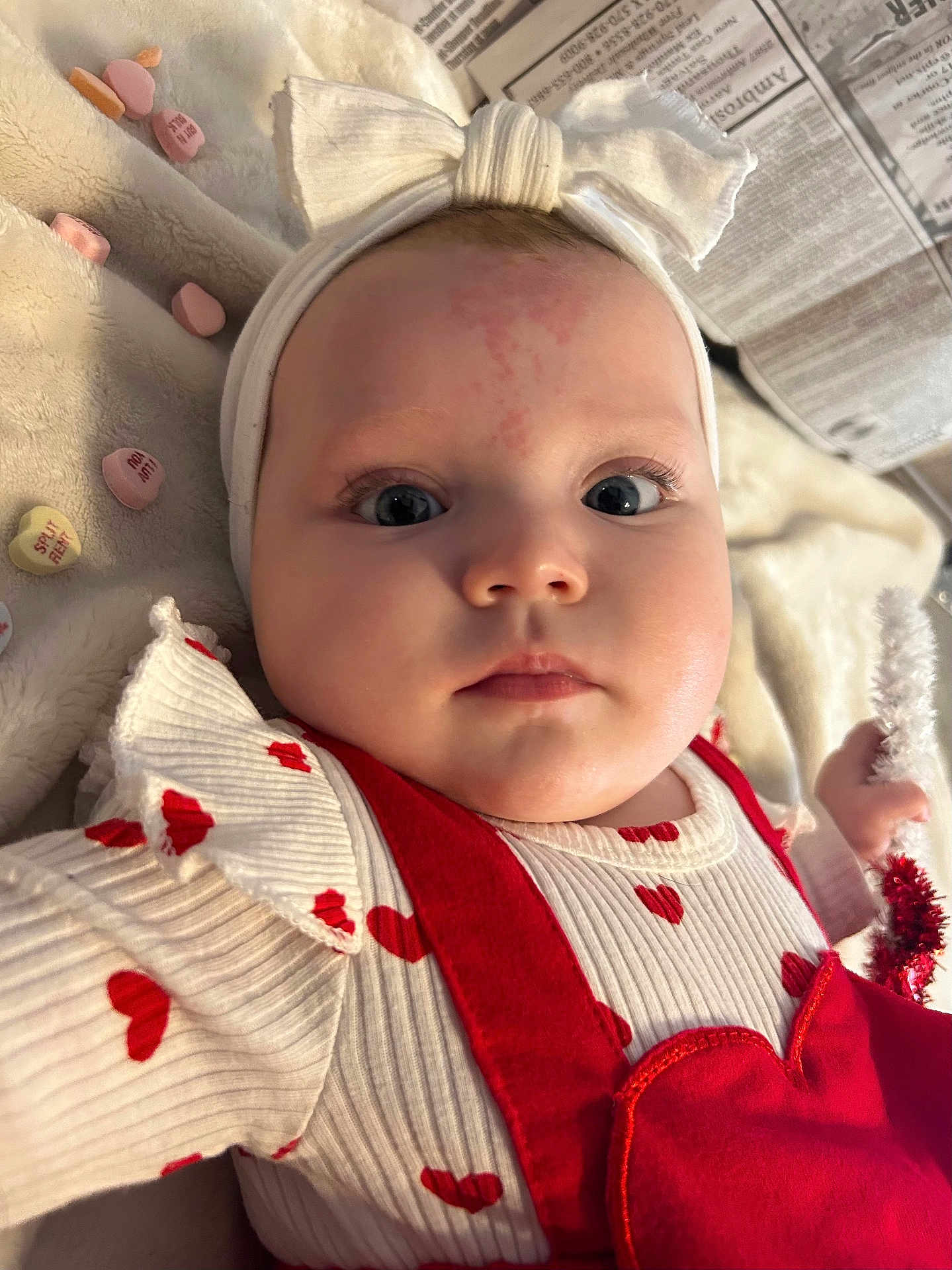 Aspyn is registered to the contest to win money with this photo: baby, infant, headband, bow, blanket, valentine_candy, heart_pattern, red_outfit, close_up, portrait, big_eyes, cheeks, lying_down, soft_texture, newspaper, plush, hand, skin_mark, curious_gaze, cute_expression