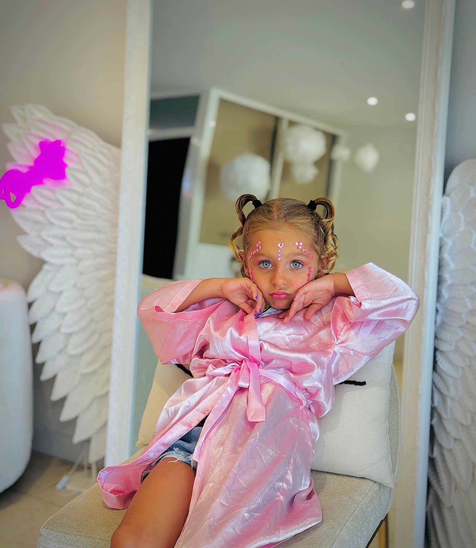 Aria a rejoint le concours — aidez-le/la à gagner de superbes lots ! child, girl, pink_robe, denim_shorts, face_jewels, pouting, chair, mirror, angel_wings, indoor, curly_hair, blue_eyes, decorations, white, soft_lighting, portrait, fashion, playful, seated, home