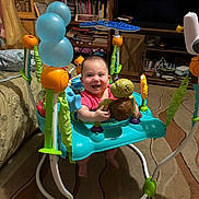 Journie joined the competition — help win amazing prizes! baby, smiling, activity_jumper, toy, indoor, carpet, furniture, bookshelf, television, living_room, child, play, colorful, happy, floor, person, plastic, seat, foot, head
