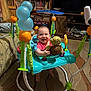 baby, smiling, activity_jumper, toy, indoor, carpet, furniture, bookshelf, television, living_room, child, play, colorful, happy, floor, person, plastic, seat, foot, head