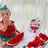 baby, child, watermelon, fruit, plate, ice_cubes, orange_fruit, sign, summer, clothing, headband, sitting, food, snack, cute, indoor, white_background, portrait, colorful, happy