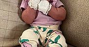 Ameliana is registered to the contest to win money with this photo: baby, bow, child, comfortable, couch, cozy, cute, fashion, floral_pants, happy, headband, indoor, infant, mittens, person, portrait, purple_shirt, sitting, smiling, soft_lighting