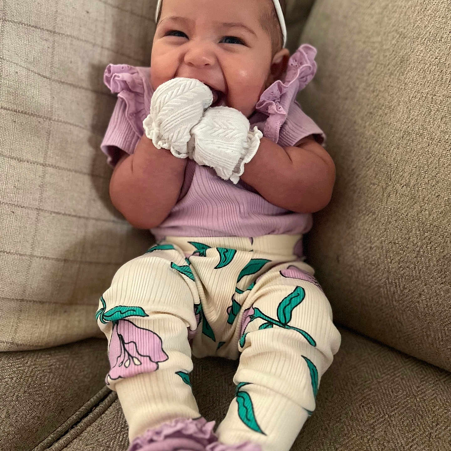 Ameliana is registered to the contest to win money with this photo: baby, bow, child, comfortable, couch, cozy, cute, fashion, floral_pants, happy, headband, indoor, infant, mittens, person, portrait, purple_shirt, sitting, smiling, soft_lighting