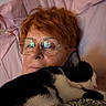 bed, black_and_white_cat, cat, close_up, comfort, cozy, eyewear, glasses, indoor, nap, person, pet, pillow, portrait, red_hair, relaxation, resting, sleeping, snuggling, soft_lighting